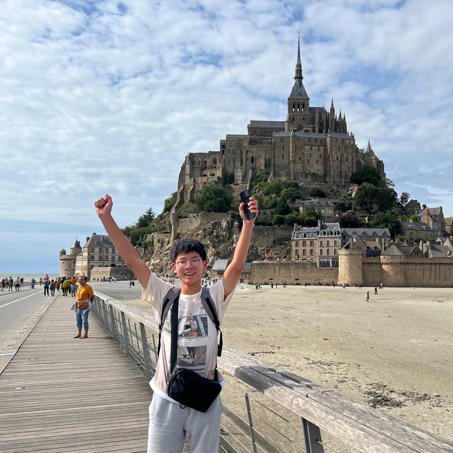 Ethan cheering with both arms up on the walkway in front of Mont-Saint-Michel