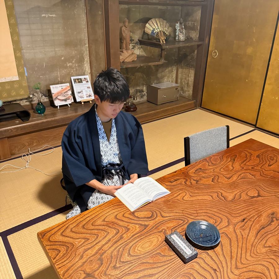 Ethan in a yukata reading a book at a wooden table in a tatami room