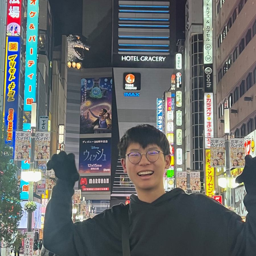 Ethan doing a monster pose on a neon-lit street in Shinjuku, with the Godzilla head on a building behind him