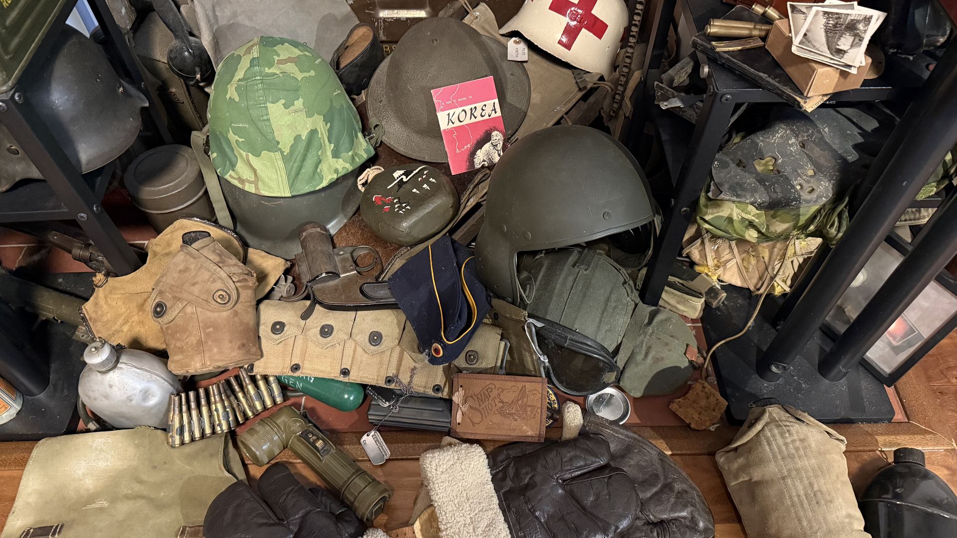 A large pile of military artifacts from Ethan's collection: helmets, a medic's helmet with a red cross, canteens, gas masks, ammunition, pouches, and field gear