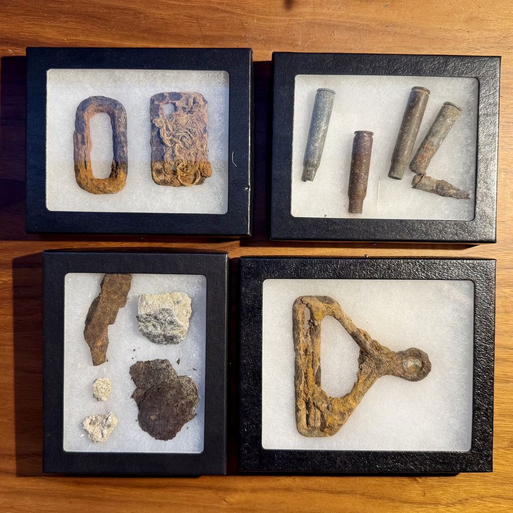 Four display boxes of rusted, excavated metal relics and spent cartridges from Normandy