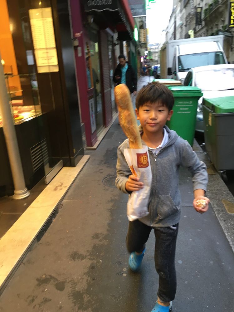Young Ethan walking down a Paris street carrying a baguette
