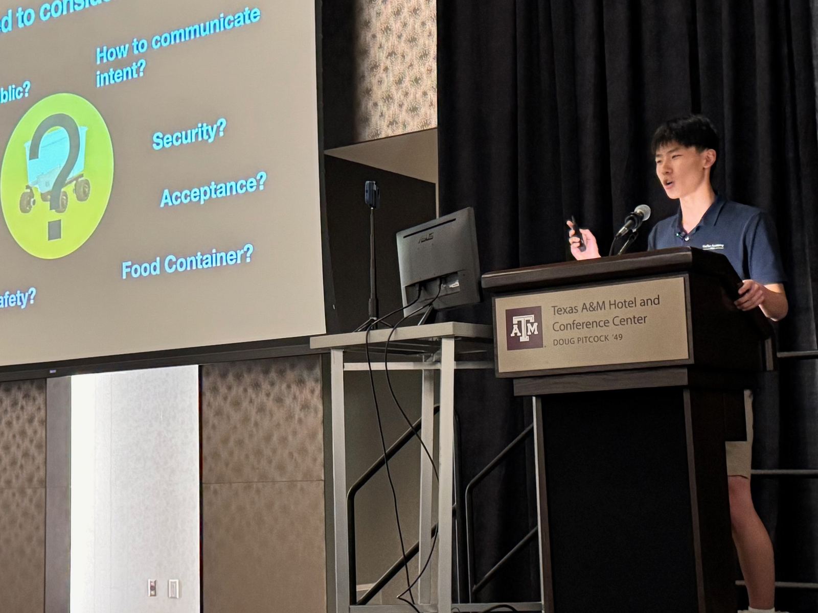 Ethan speaking at a podium at the Texas A&M Hotel and Conference Center, beside a slide of design questions for Food Angel