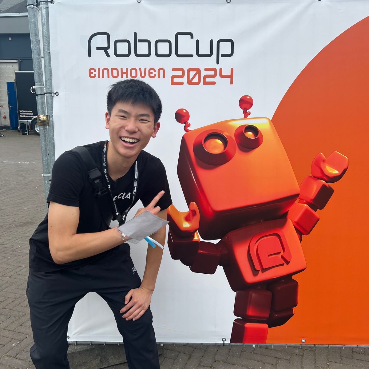 Ethan laughing and pointing at the RoboCup Eindhoven 2024 sign with its orange robot mascot