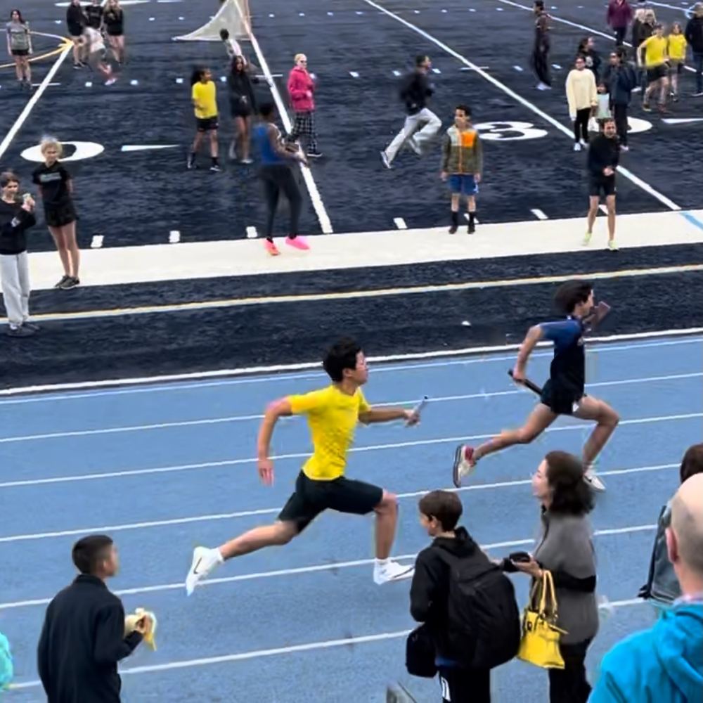 Ethan in a yellow shirt sprinting with a relay baton as spectators watch
